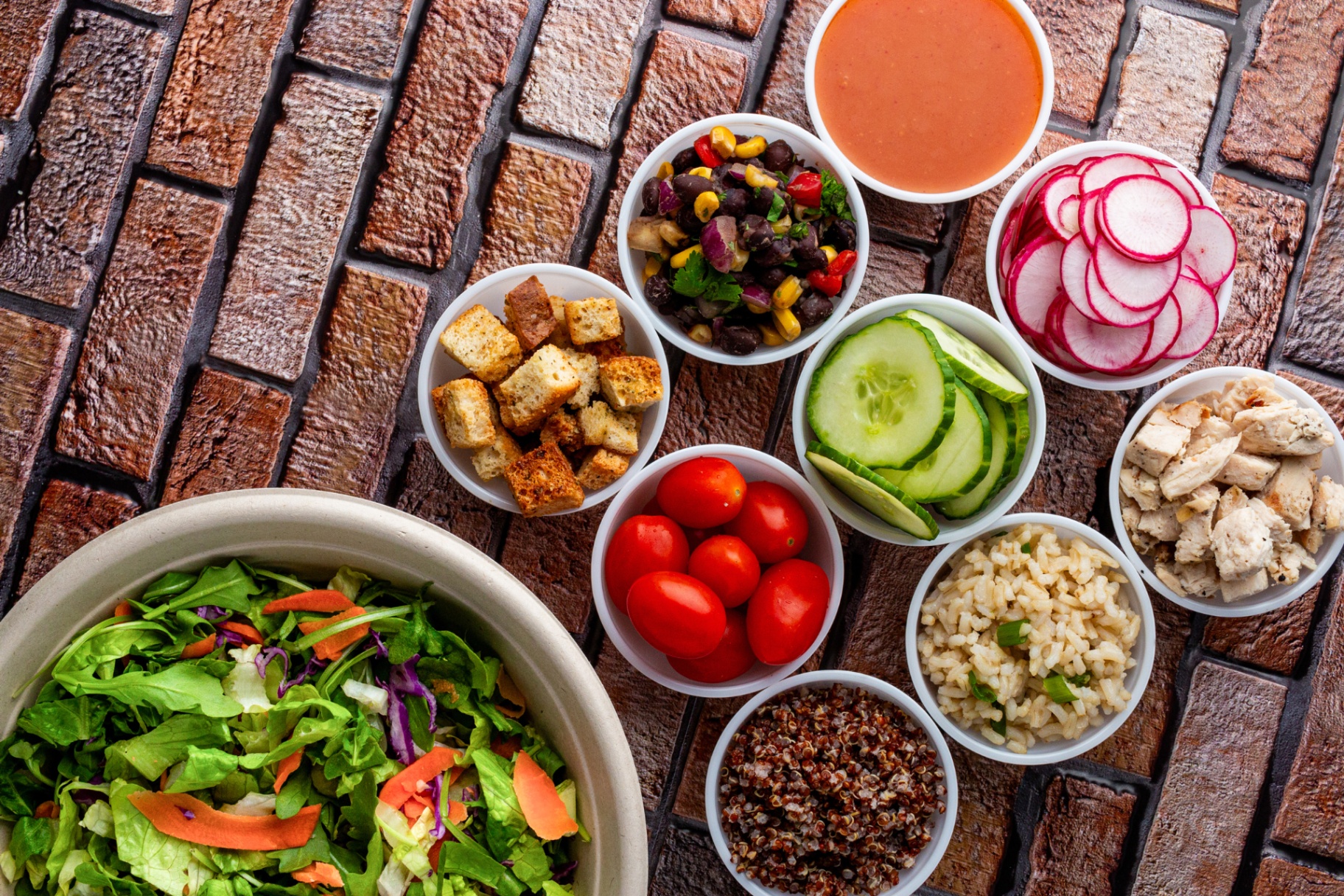 A build-your-own bowl spread with fresh ingredients on a brick surface